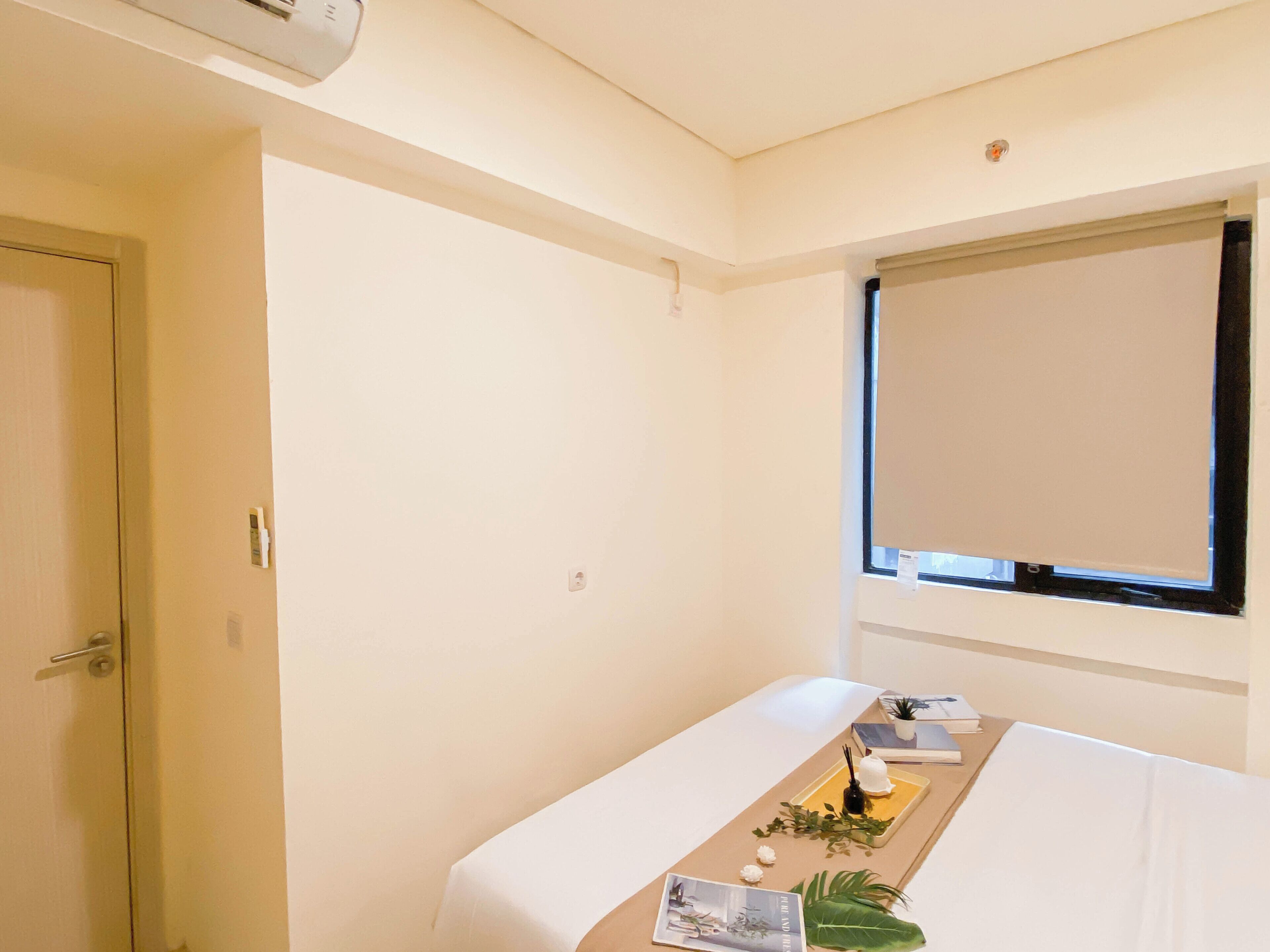 A hotel room with a bed, a window with a blind, a small table with a tray of items, and a door.