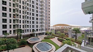 A high-rise building with multiple balconies and a courtyard with circular planters and a glass-top seating area. - Simple Style Studio Apartment (No Kitchen) At Tokyo Riverside Pik 2 (Teluknaga)