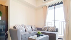 A modern living room with a grey sofa set, a glass coffee table, and a small plant. - Soft Scandinavian 3Br At Meikarta Apartment (Cikarang)