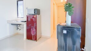 A compact kitchen with a refrigerator, microwave, sink, and a potted plant. - Soft Scandinavian 3Br At Meikarta Apartment (Cikarang)