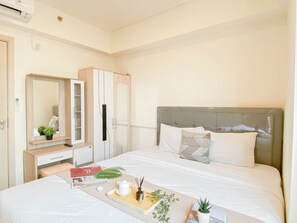 A hotel room with a bed, bedside table, dresser, and a large mirror. - Soft Scandinavian 3Br At Meikarta Apartment (Cikarang)