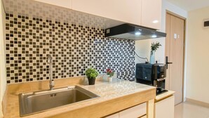A modern kitchen with a tiled backsplash, stainless steel sink, and a black range hood. - 3Br Apartment Near Dian Harapan School At Meikarta (Cikarang)