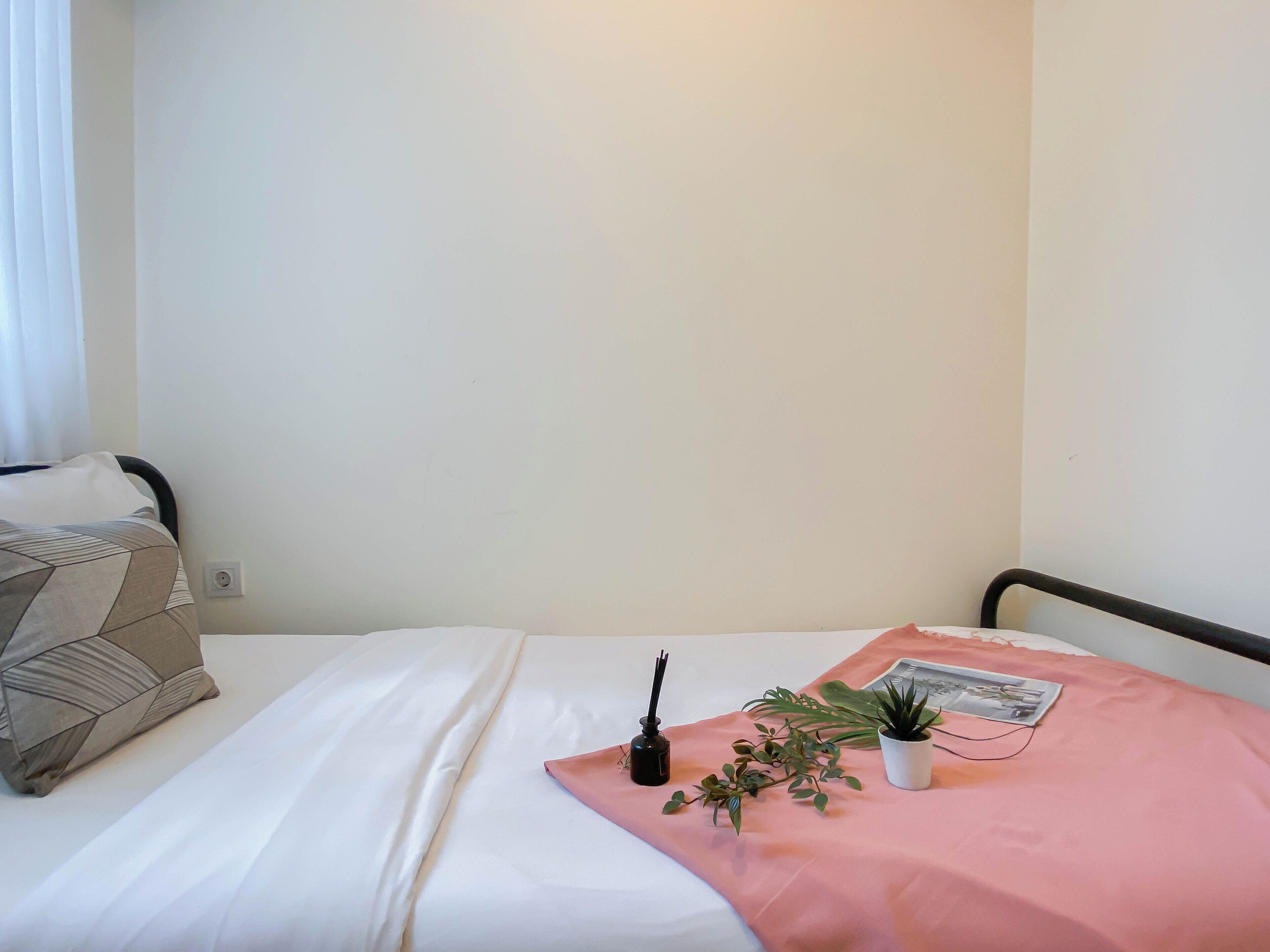 A neatly made bed with a white sheet and a pink blanket, a small potted plant, and a magazine on the bed.