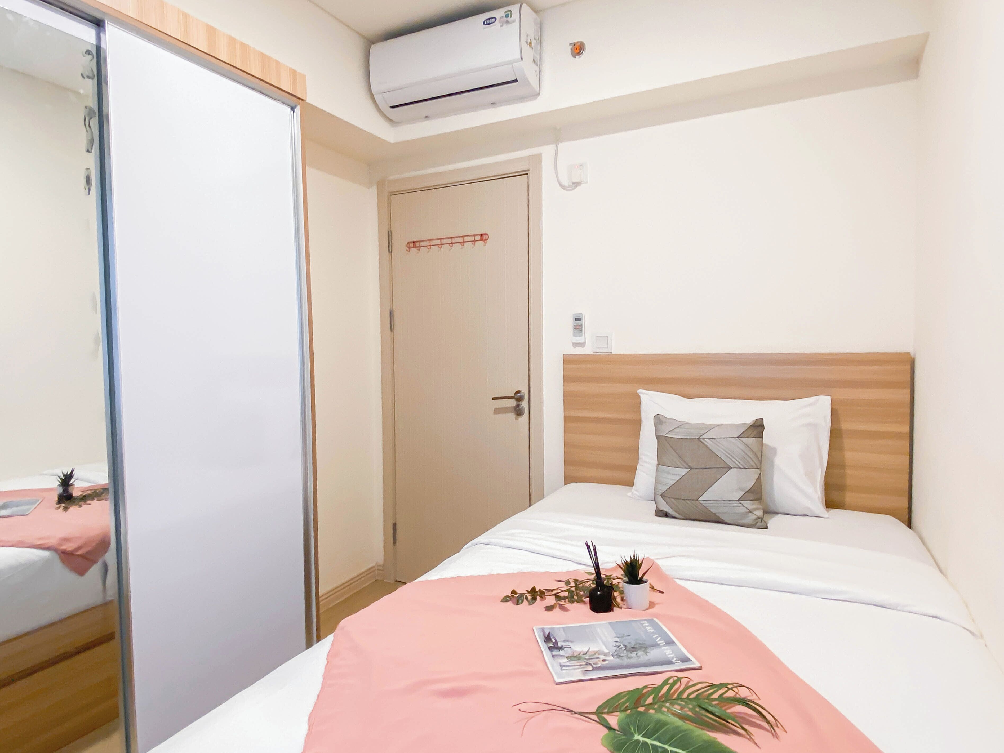 Et hotelværelse med en seng, et natbord med et magasin, en lille stueplante og en aircondition-enhed på væggen.