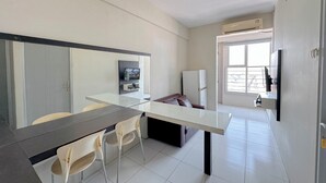 A modern kitchen with a glass dining table, two chairs, a refrigerator, and a TV mounted on the wall. - Strategic 2Br Apartment Near Its Campus At Dian Regency (Surabaya)
