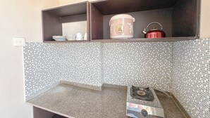 A kitchen with a tiled backsplash, a stove, a kettle, and a rice cooker on a shelf. - Strategic 2Br Apartment Near Its Campus At Dian Regency (Surabaya)