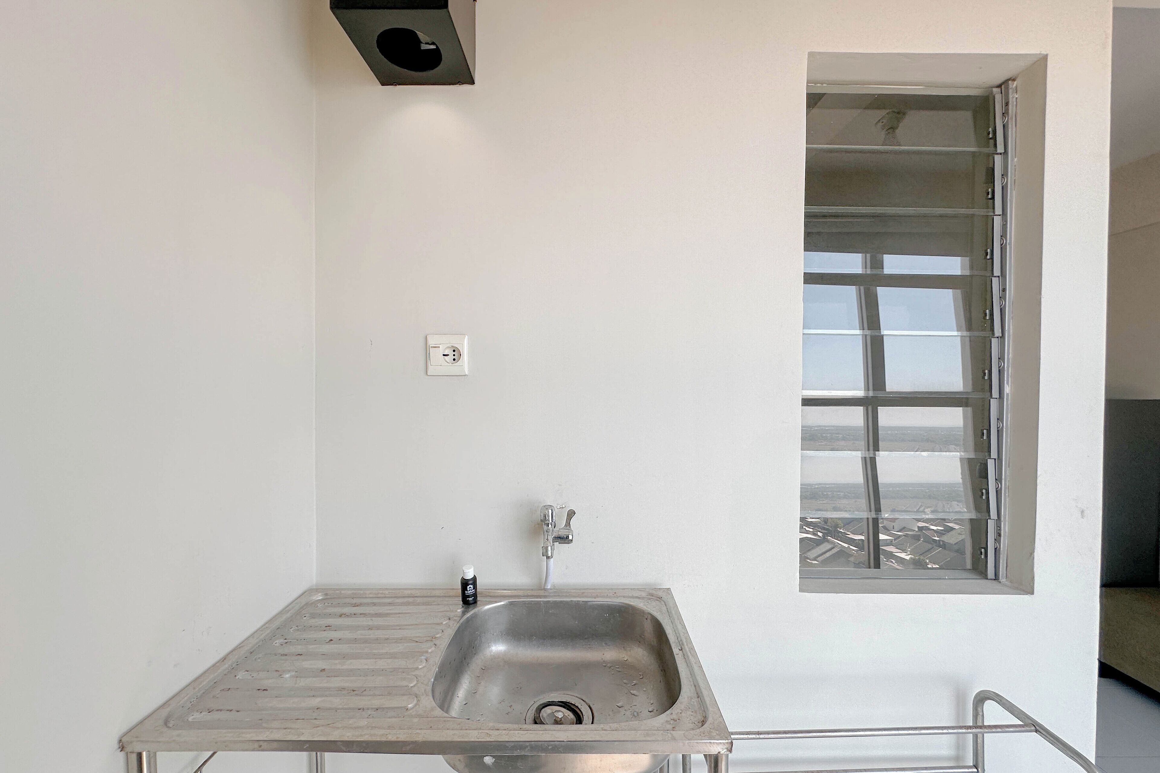 Een kleine badkamer met een metalen wastafel, een kraan, een raam met uitzicht en een stopcontact.
