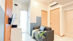 Et moderne, godt oplyst rum med en grå sofa, et lille skrivebord med en computer og et stort vindue.