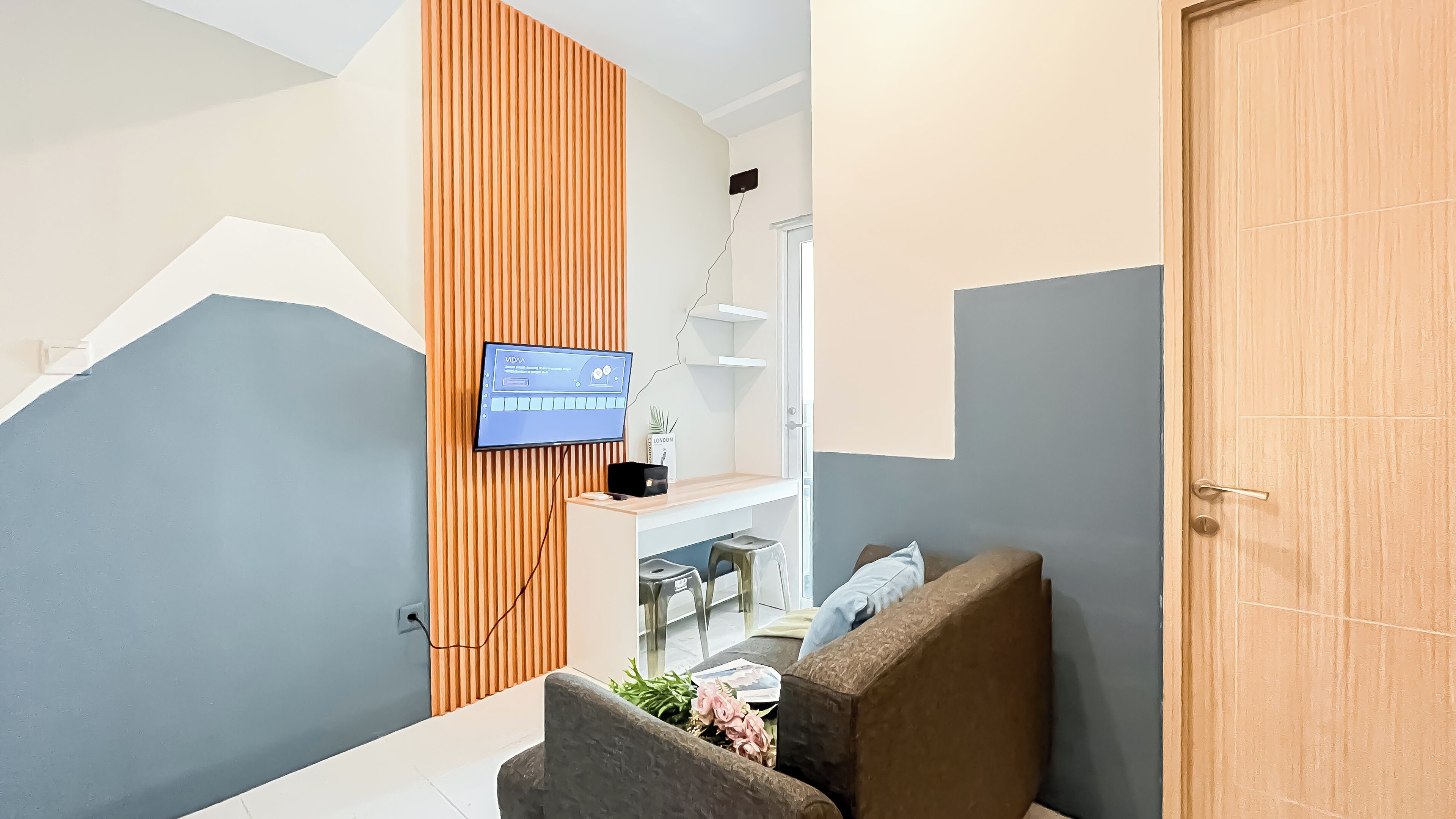 A modern reception area with a flat-screen TV mounted on a wooden panel, a seating area with a sofa and cushions, and a door to the right.