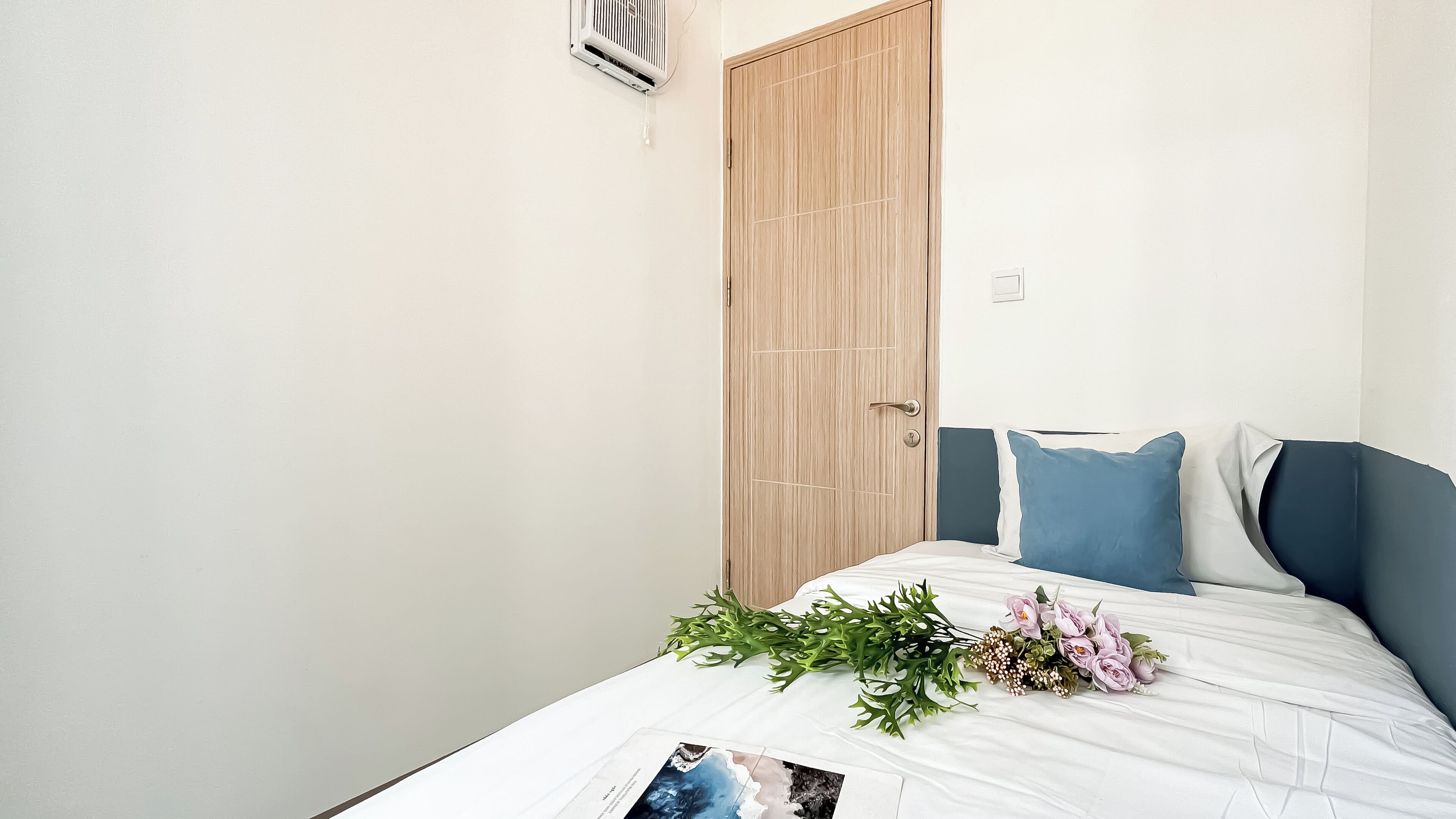 A bedroom with a bed, a wooden door, and a wall-mounted air conditioner.