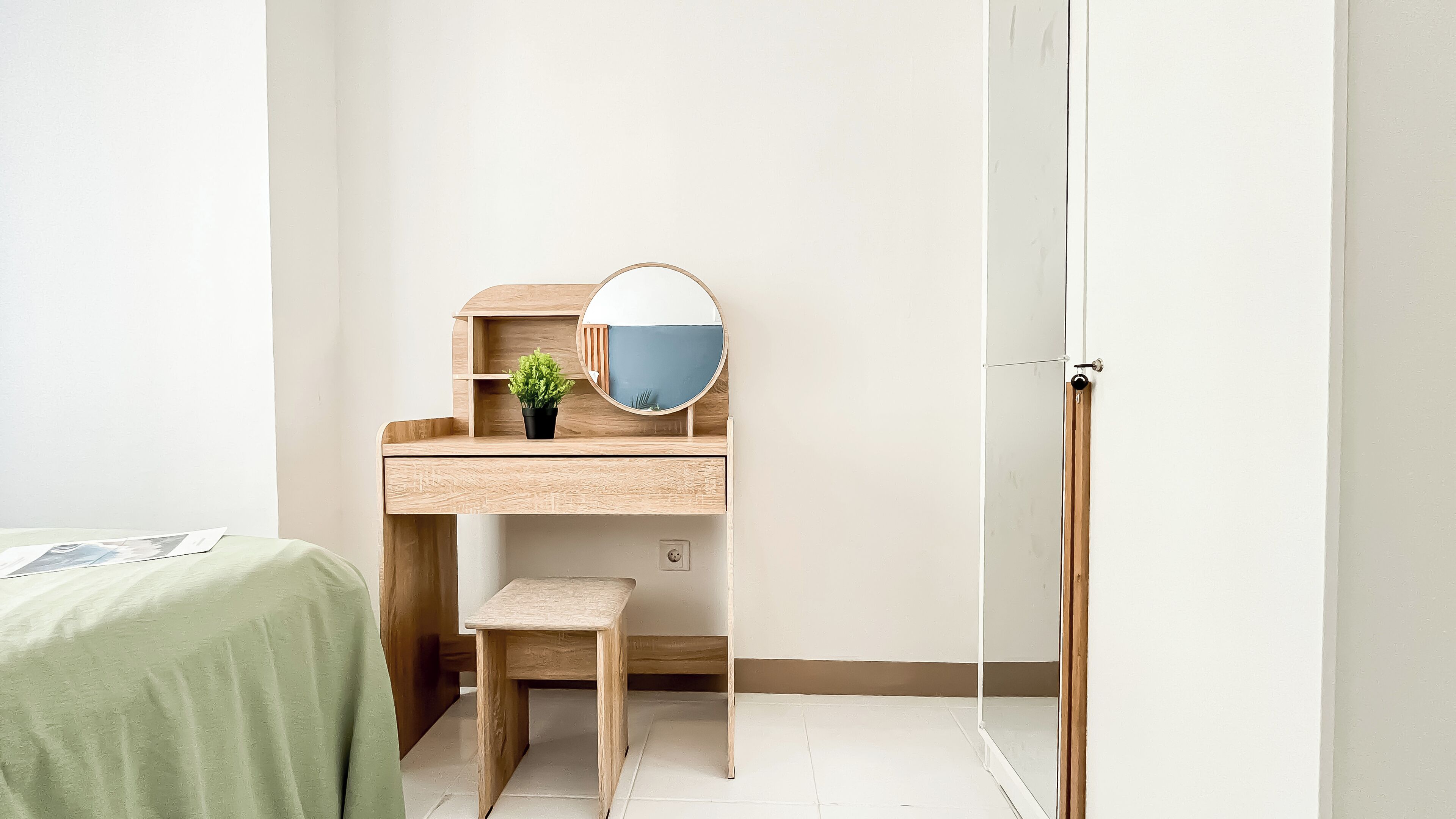 A compact bedroom with a wooden desk, a small stool, a potted plant, and a mirror.