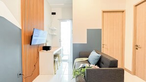 En moderne stue med et fladskærms-tv monteret på en væg af træpaneler, en sofa med en pude, og en trädør.