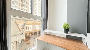 A balcony with a wooden table and a potted plant, overlooking a busy street and buildings. - Soft Industrial Look Studio At Tokyo Riverside Pik 2 Apartment (Teluknaga)
