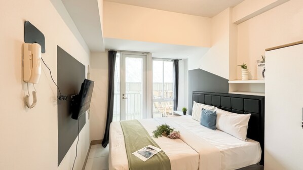 A hotel room with a bed, a telephone, a television, and a window with curtains. - Soft Industrial Look Studio At Tokyo Riverside Pik 2 Apartment (Teluknaga)