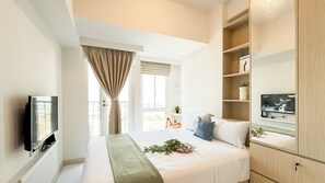 Une chambre à coucher avec un lit, une télévision, une fenêtre avec des rideaux et une étagère ornée d’objets décoratifs.
