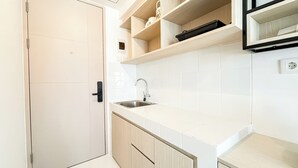 A modern kitchen with white cabinets, a stainless steel sink, and wooden shelves. - Basic Studio Room Apartment Tokyo Riverside Pik 2 (Teluknaga)