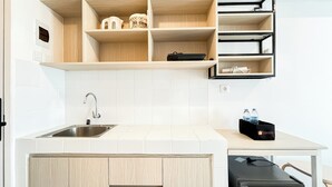A modern kitchen with a stainless steel sink, white tiled backsplash, wooden cabinets, and a black countertop. - Basic Studio Room Apartment Tokyo Riverside Pik 2 (Teluknaga)