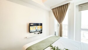 A hotel room with a bed, a mounted TV on the wall, and a window with curtains. - Basic Studio Room Apartment Tokyo Riverside Pik 2 (Teluknaga)