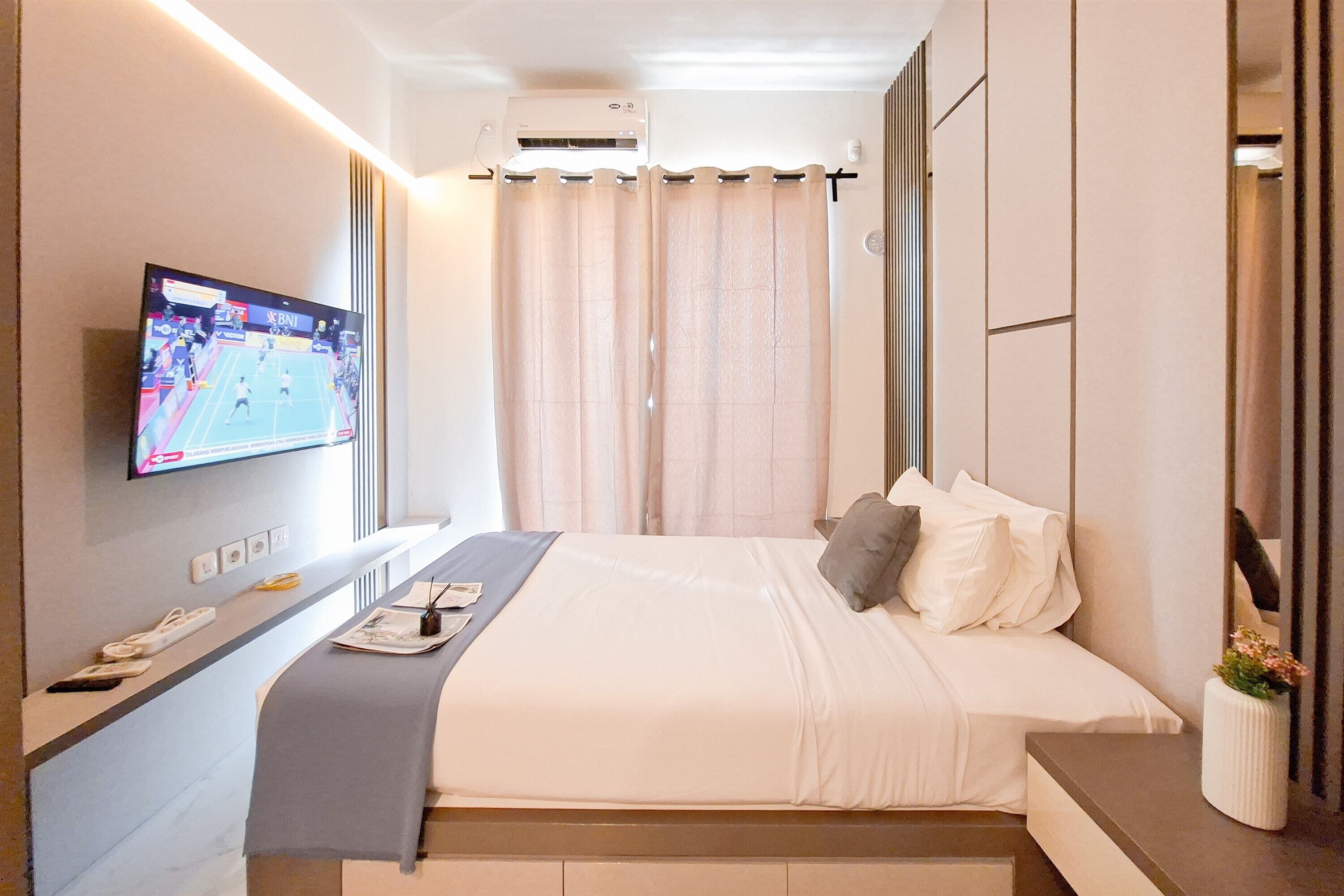 A hotel room with a bed, bedside table, TV, and a curtain.