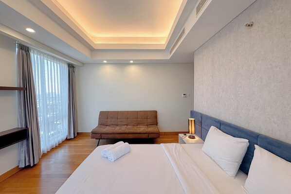 Una habitación de hotel con cama, sofá, mesita de noche con lámpara y ventana con cortinas.