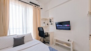 Una camera d'albergo con un letto, una scrivania, una sedia, una televisione e una finestra con tende.