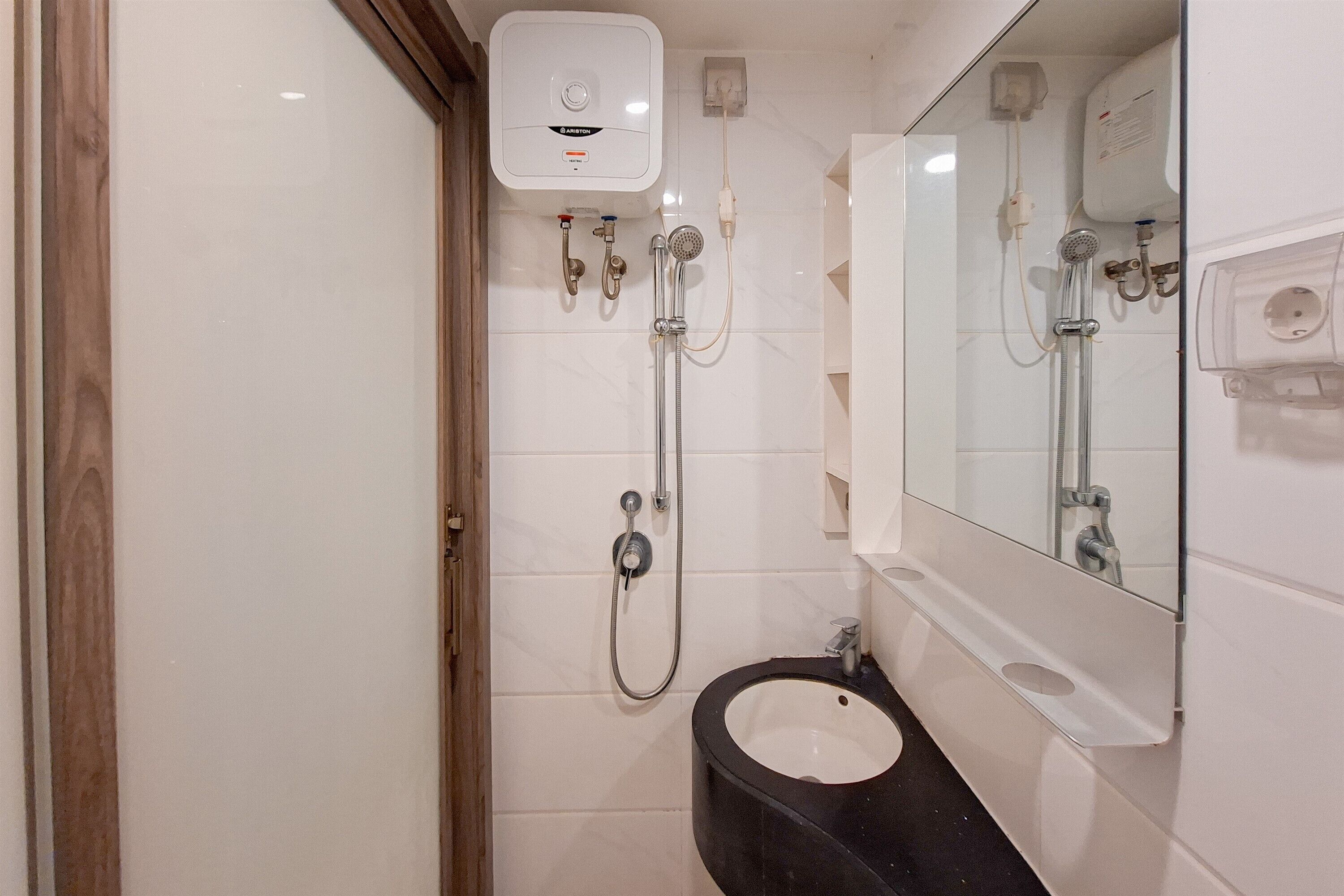 Une salle de bain avec un mur recouvert de carreaux blancs, un lavabo noir, un miroir et une douche dotée d’un panneau de commande situé au-dessus.