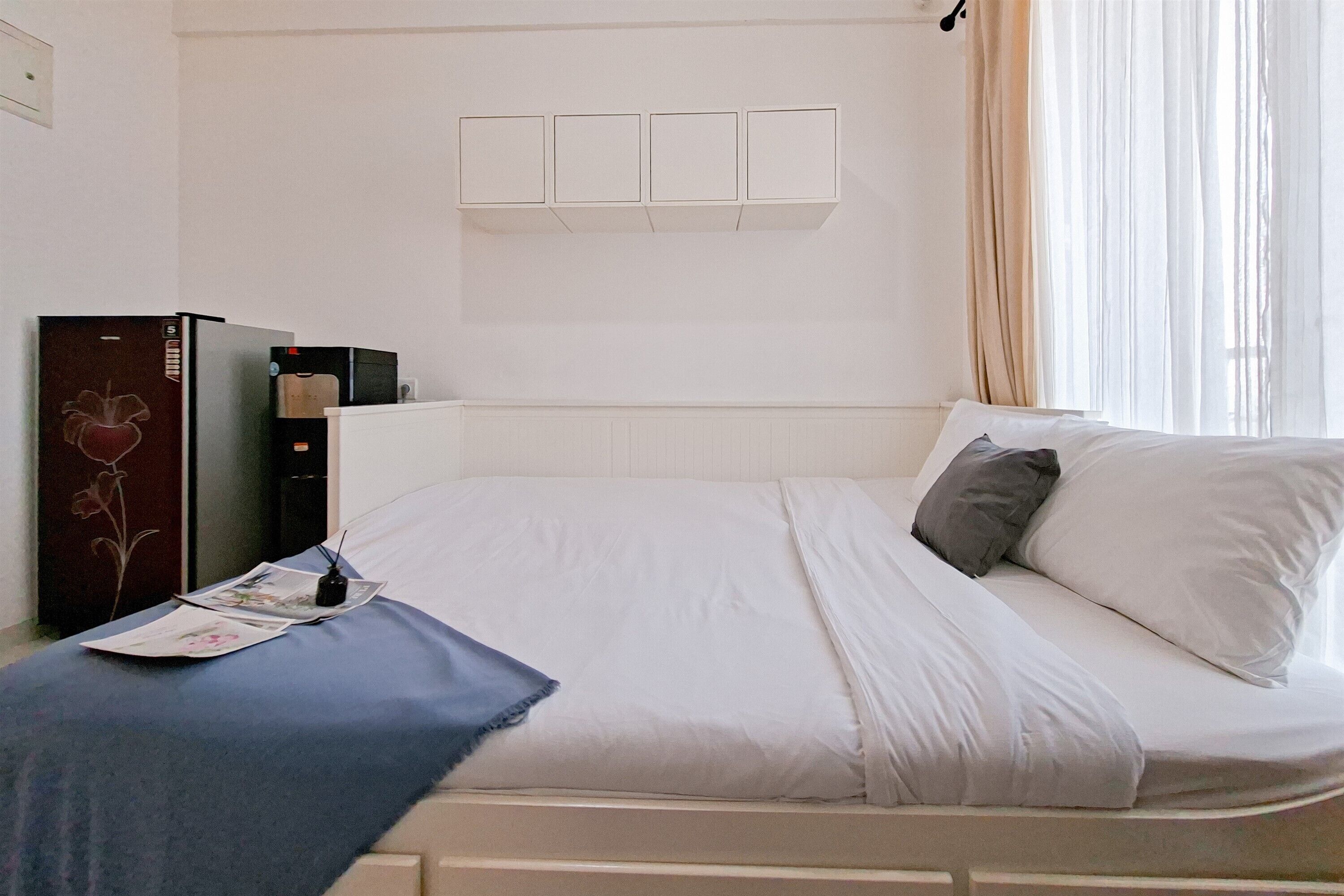 Een hotelkamer met een bed, nachtkastje, bureau en een wandplank.