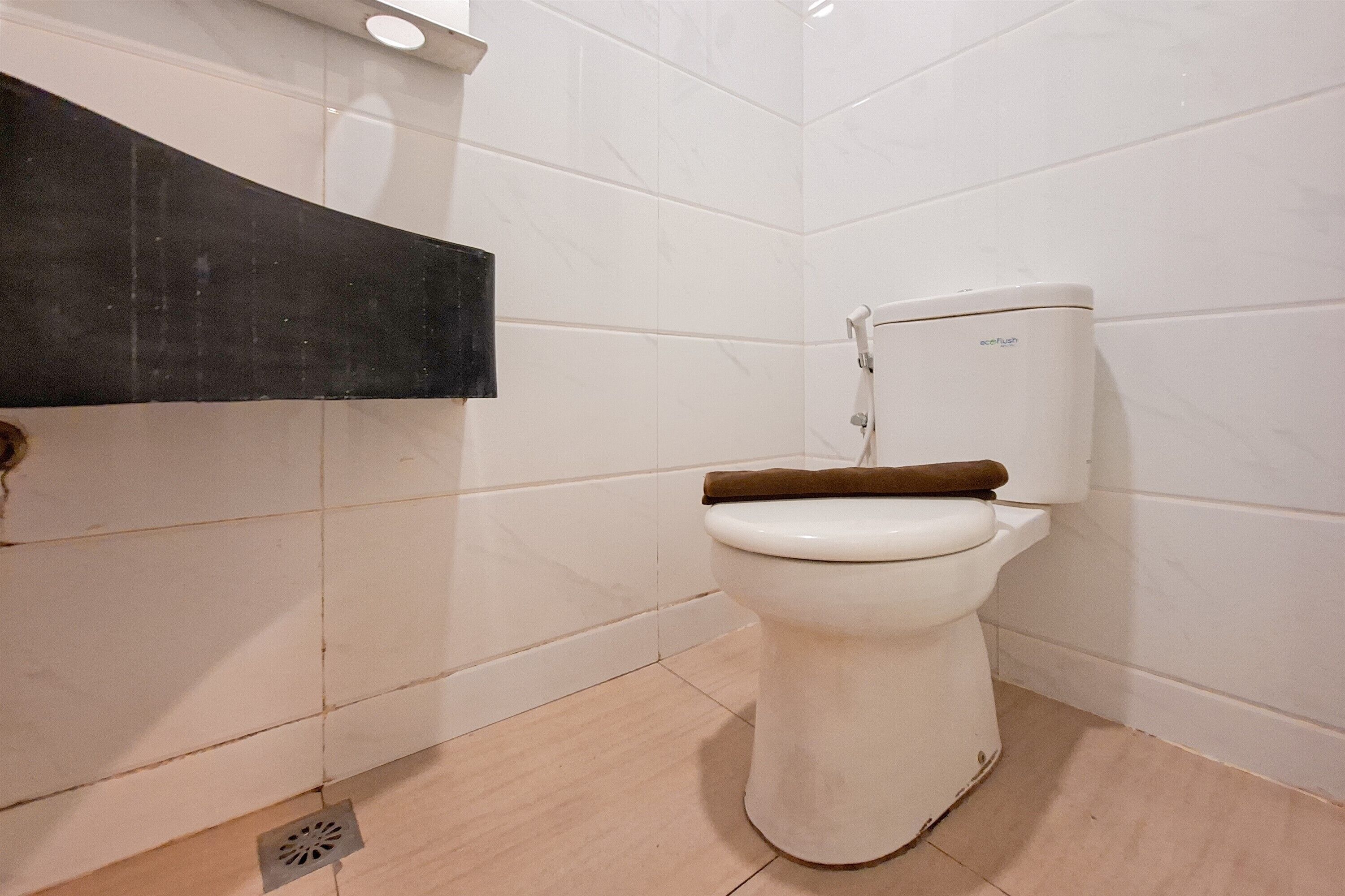 Une salle de bain avec des toilettes blanches, une étagère noire et un sol carrelé.