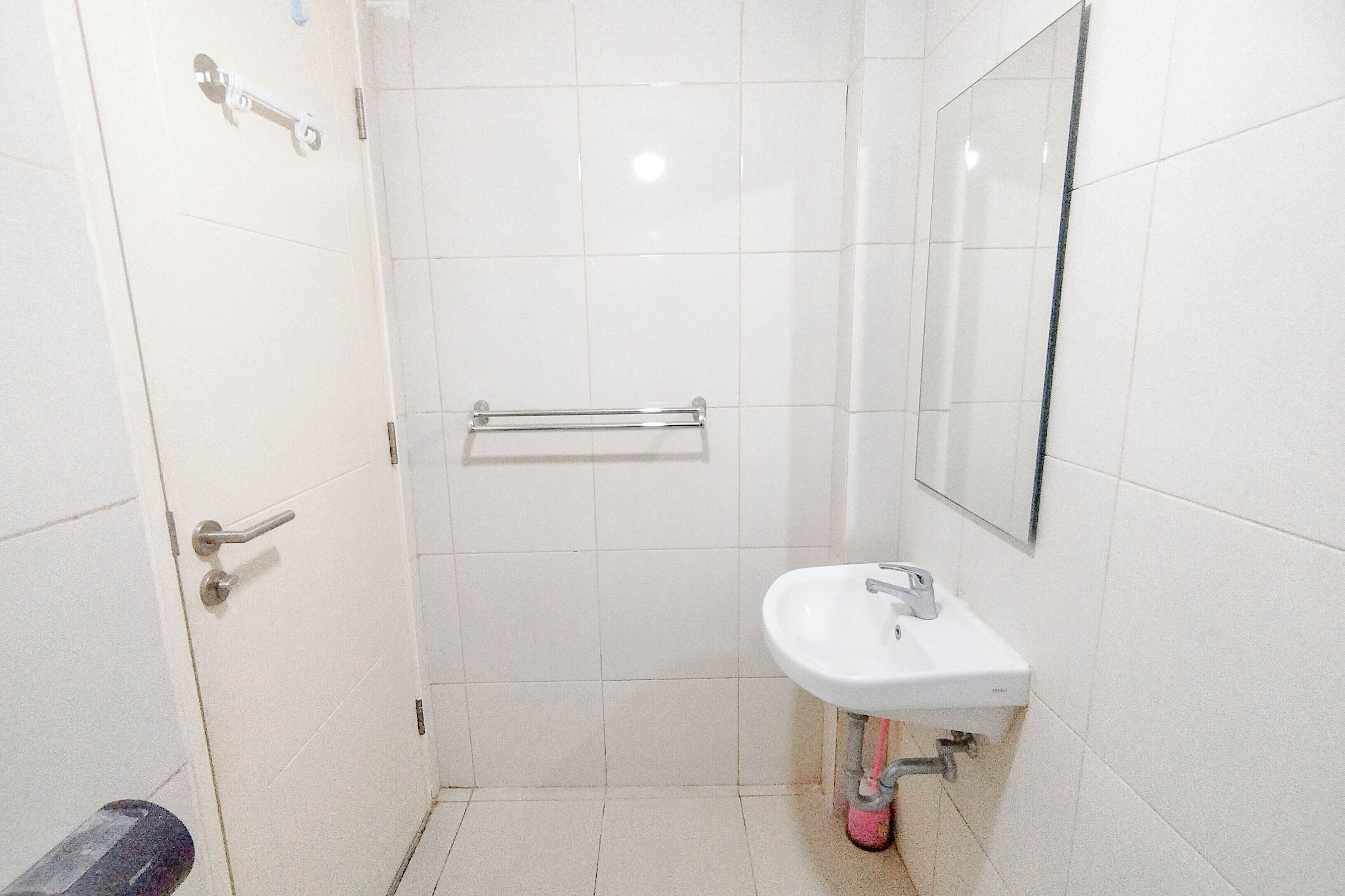 A small, clean bathroom with a white sink, a mirror, and a handrail.