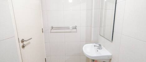 A small, clean bathroom with a white sink, a mirror, and a handrail.