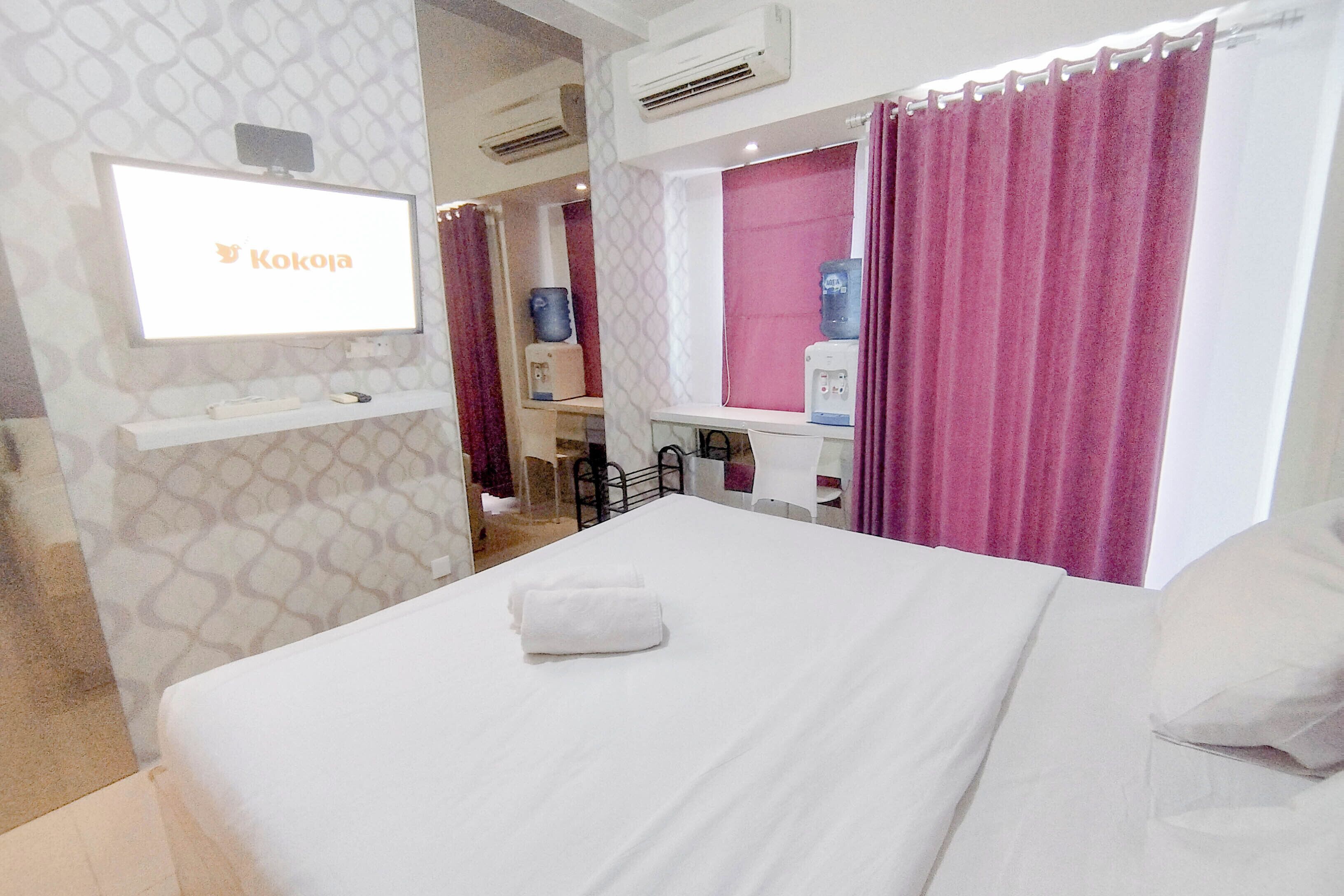Una camera d'albergo con un letto, una TV a parete, un dispenser d'acqua e un angolo doccia.