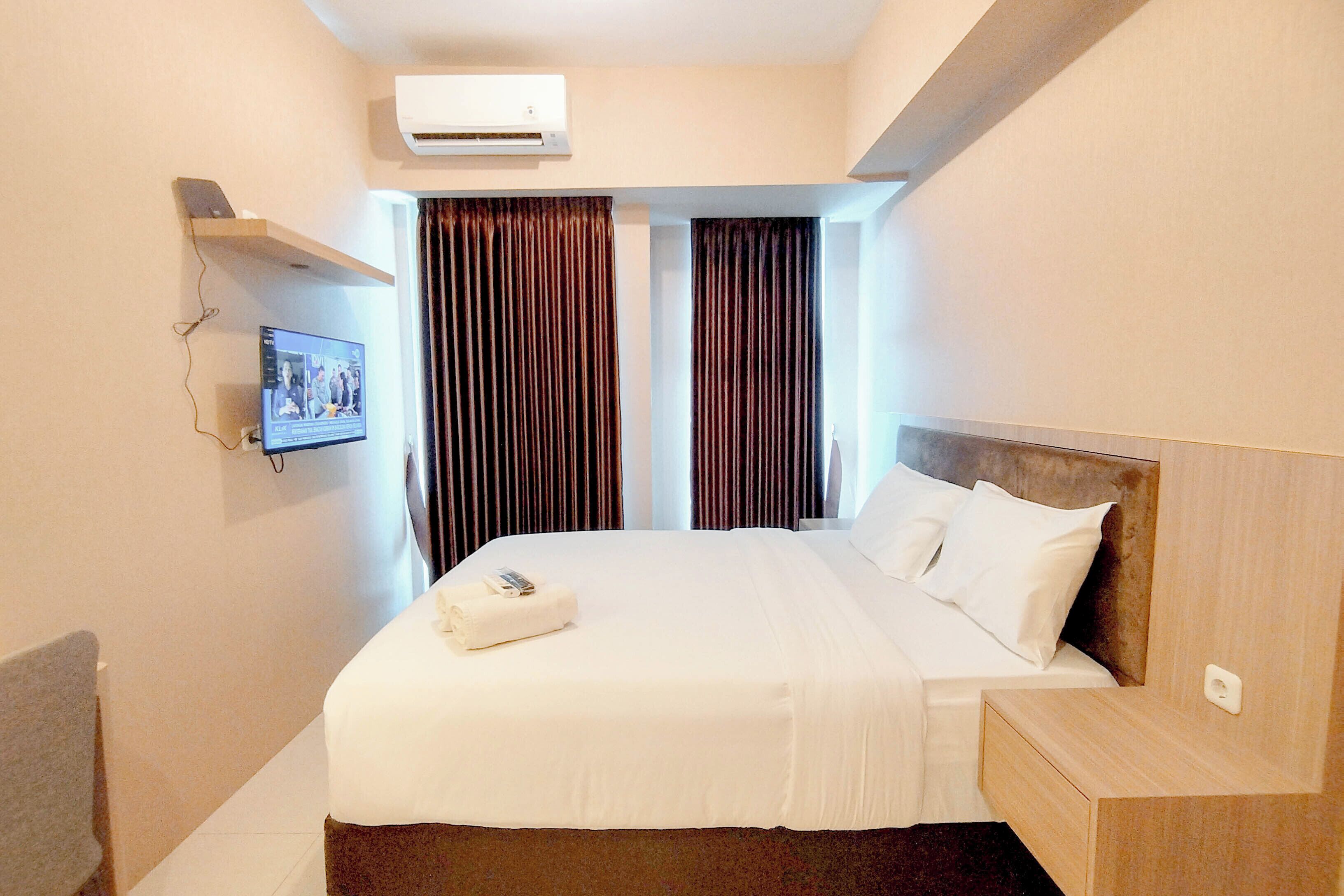 A hotel room with a bed, a bedside table, a TV mounted on the wall, and an air conditioning unit.