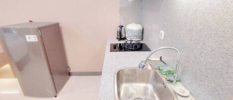 A compact kitchen with a stainless steel sink, a kettle, and a small refrigerator.