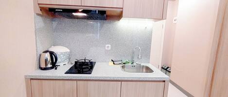 A compact kitchen with wooden cabinets, a granite countertop, a gas stove, a kettle, and a sink.