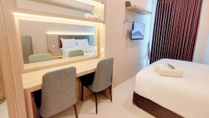 Een hotelkamer met een bed, een bureau met twee stoelen, een grote spiegel, een flatscreen televisie en een raam met gordijnen.