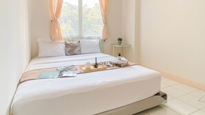A neatly made bed with pillows and a tray of toiletries, a small bedside table with a plant, and a window with curtains. - Basic 2Br Apartment Podomoro Golf View (Gunung Putri)