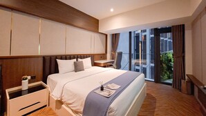 Een moderne hotelkamer met een groot bed, een nachtkastje, een klein bureau en een balkon met uitzicht op groen.