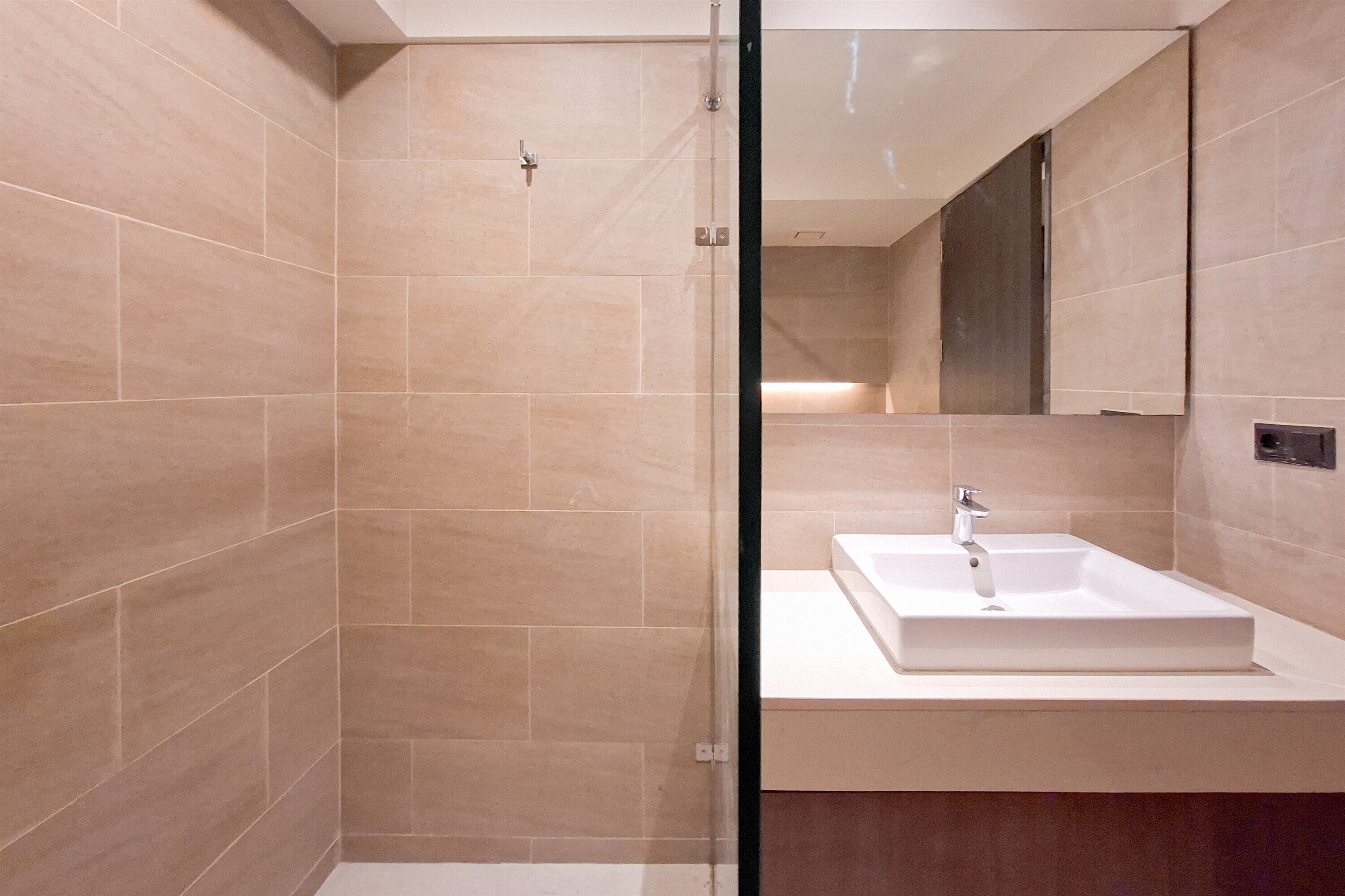 Ein modernes Badezimmer mit beigen Fliesen, einem weißen Waschbecken und einer Glasdusche.