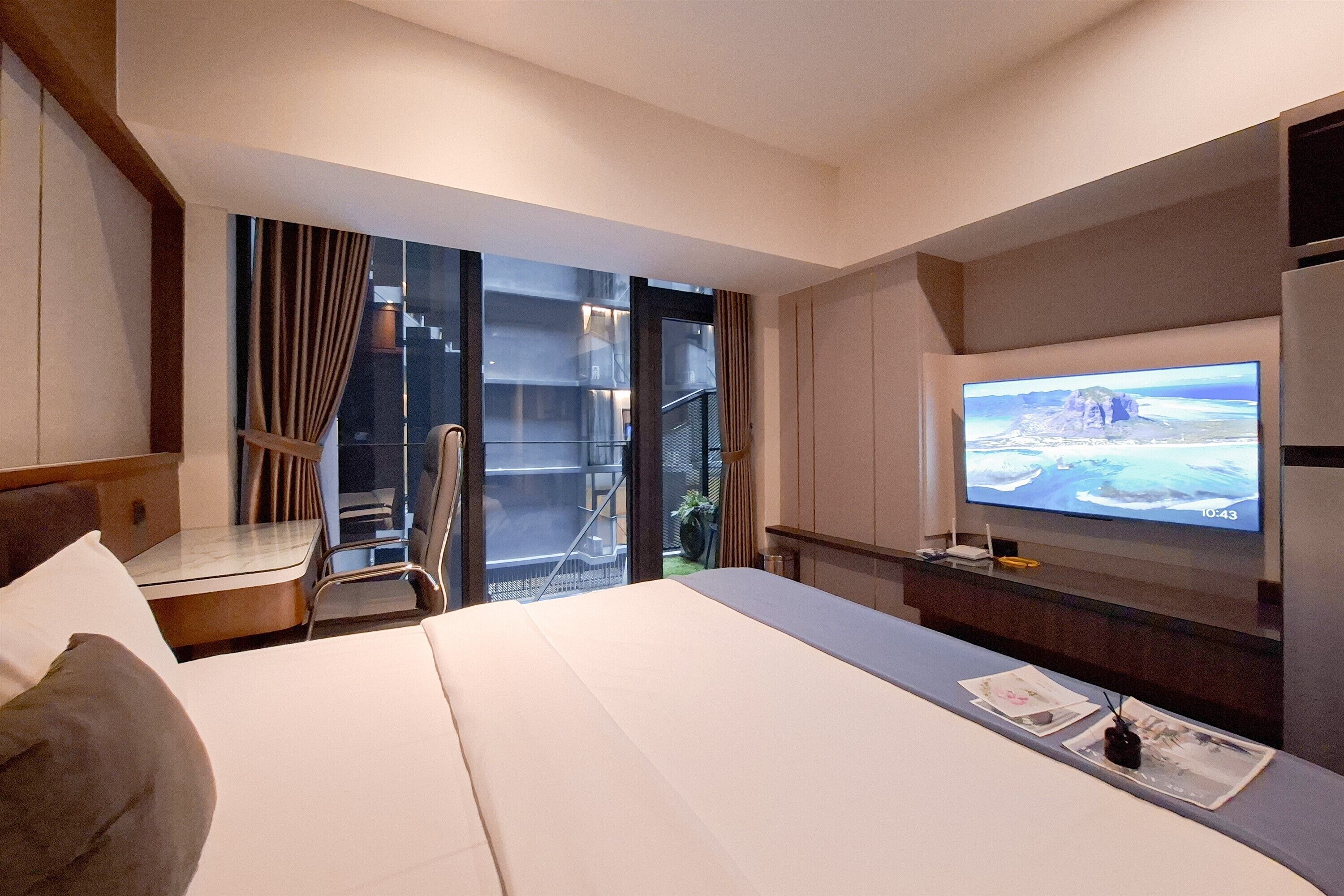 A hotel room with a bed, a desk, a TV, and a balcony with a view.