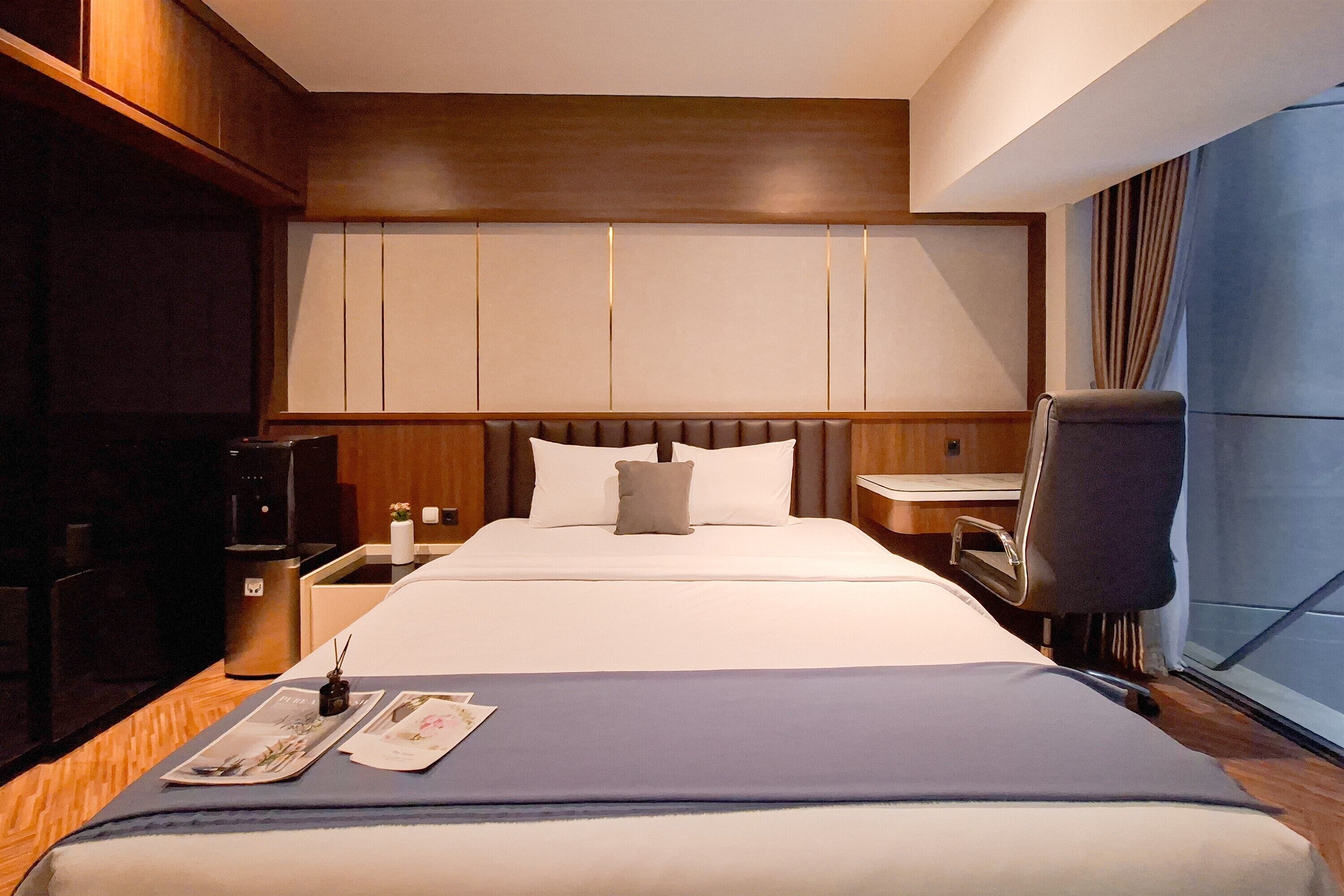 A hotel room with a large bed, wooden headboard, bedside tables, a desk, and a chair.