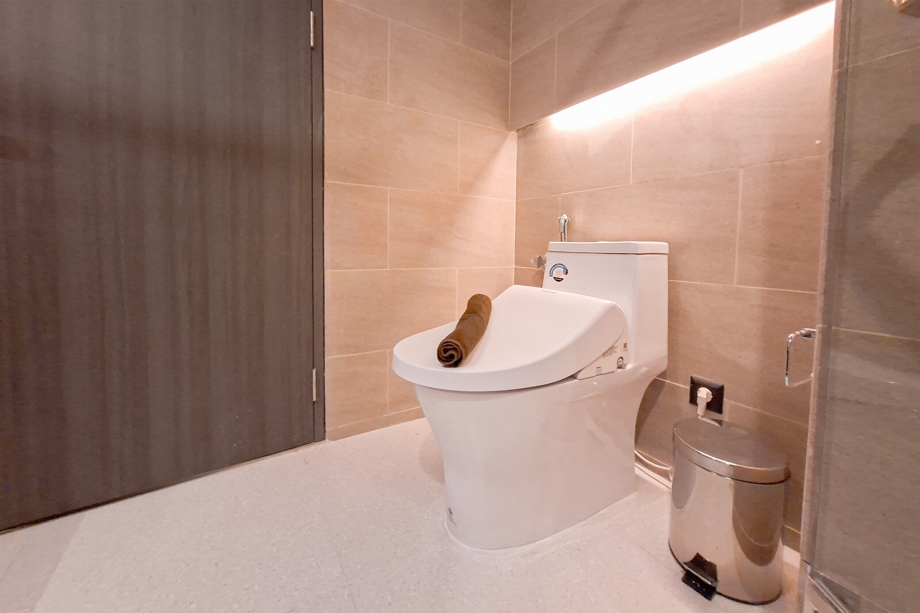 A modern bathroom with a toilet, a trash bin, and a towel on the toilet seat.