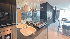 A modern kitchen with a stainless steel sink, a stove, and a glass shelf displaying kitchenware. - Spacious And Comfortable Living 3Br Apartment At Aryaduta Residence (Surabaya)