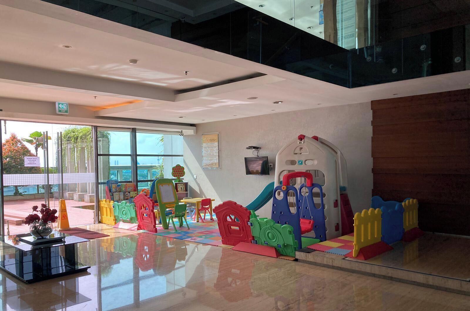 Un área de juegos interior moderna con estructuras de juego coloridas y una pared de vidrio que ofrece vistas del exterior.