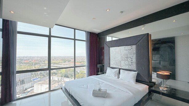 A modern hotel room with a large bed, a city view, and a unique wall art piece. - Spacious And Comfortable Living 3Br Apartment At Aryaduta Residence (Surabaya)