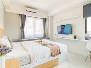 Une chambre d’hôtel moderne, équipée d’un lit, d’une télévision, d’une fenêtre avec des rideaux et d’une petite plante posée sur une étagère.