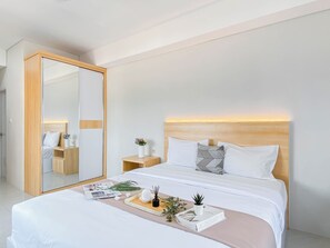 A modern hotel room with a large bed, bedside tables, a mirror, and a tray with a book and a plant. - Basic Studio At Newville Lippo Cikarang Apartment (Cikarang)