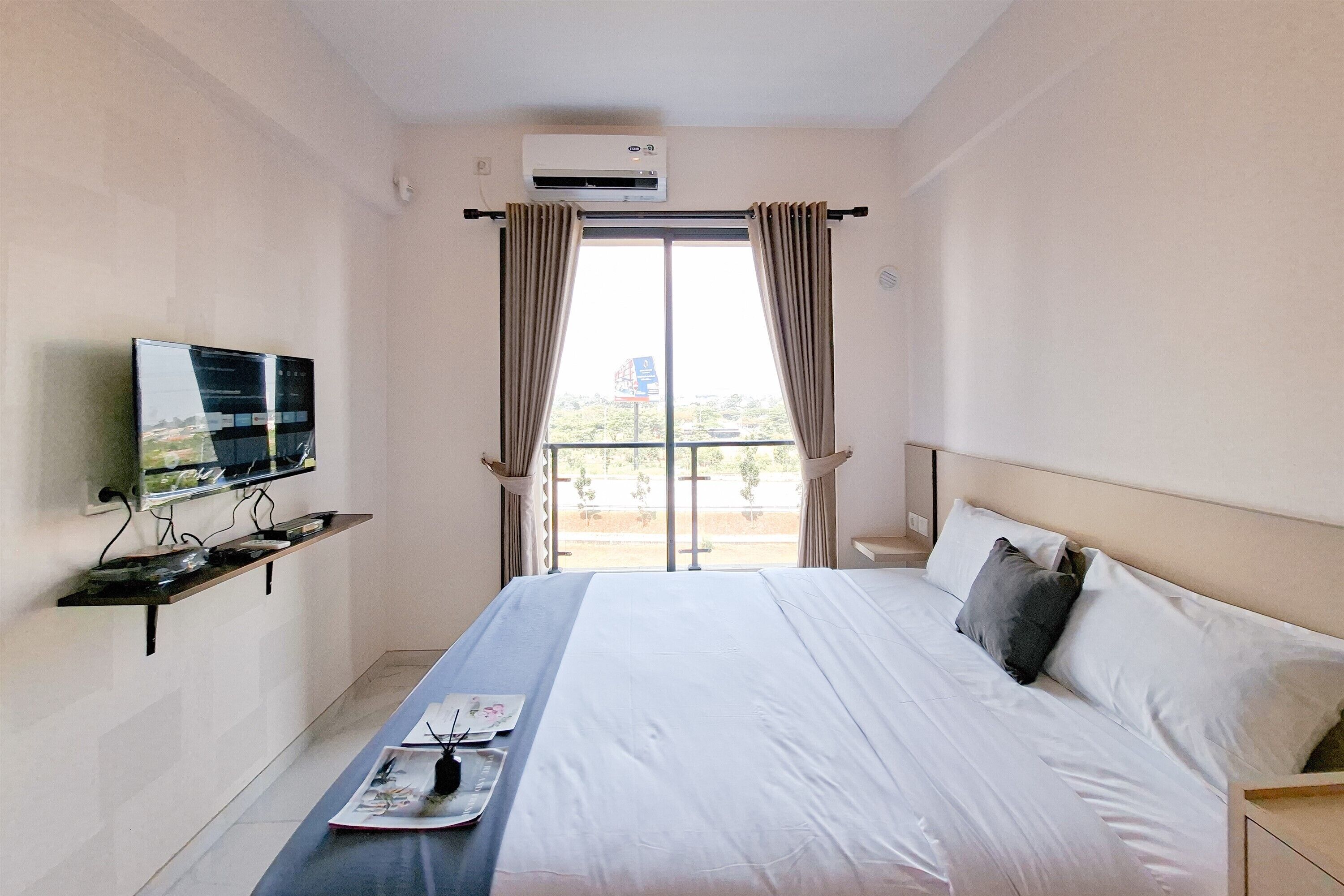 A hotel room with a bed, a flat-screen TV mounted on the wall, a window with curtains, and a balcony view.