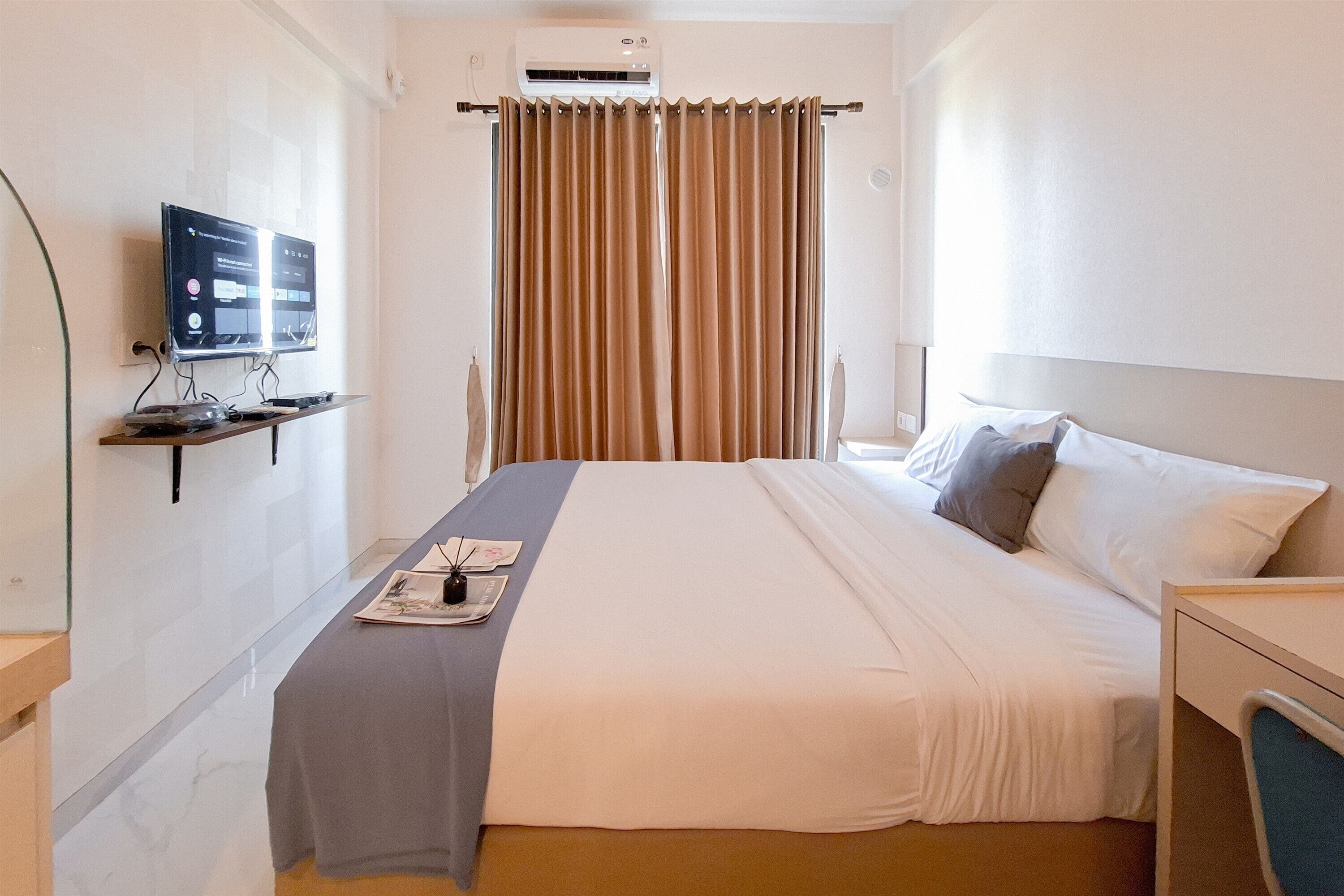 A hotel room with a bed, a TV on a stand, a desk, and a window with curtains.