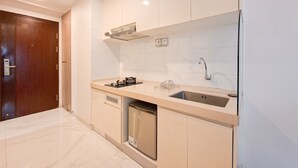 A modern kitchen with a built-in dishwasher, a stainless steel sink, and a wooden door. - Good Deal Studio At Sky House Bsd Apartment (Pagedangan)
