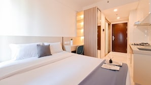 A modern hotel room with a large bed, a desk, and a bathroom visible through an open door. - Good Deal Studio At Sky House Bsd Apartment (Pagedangan)